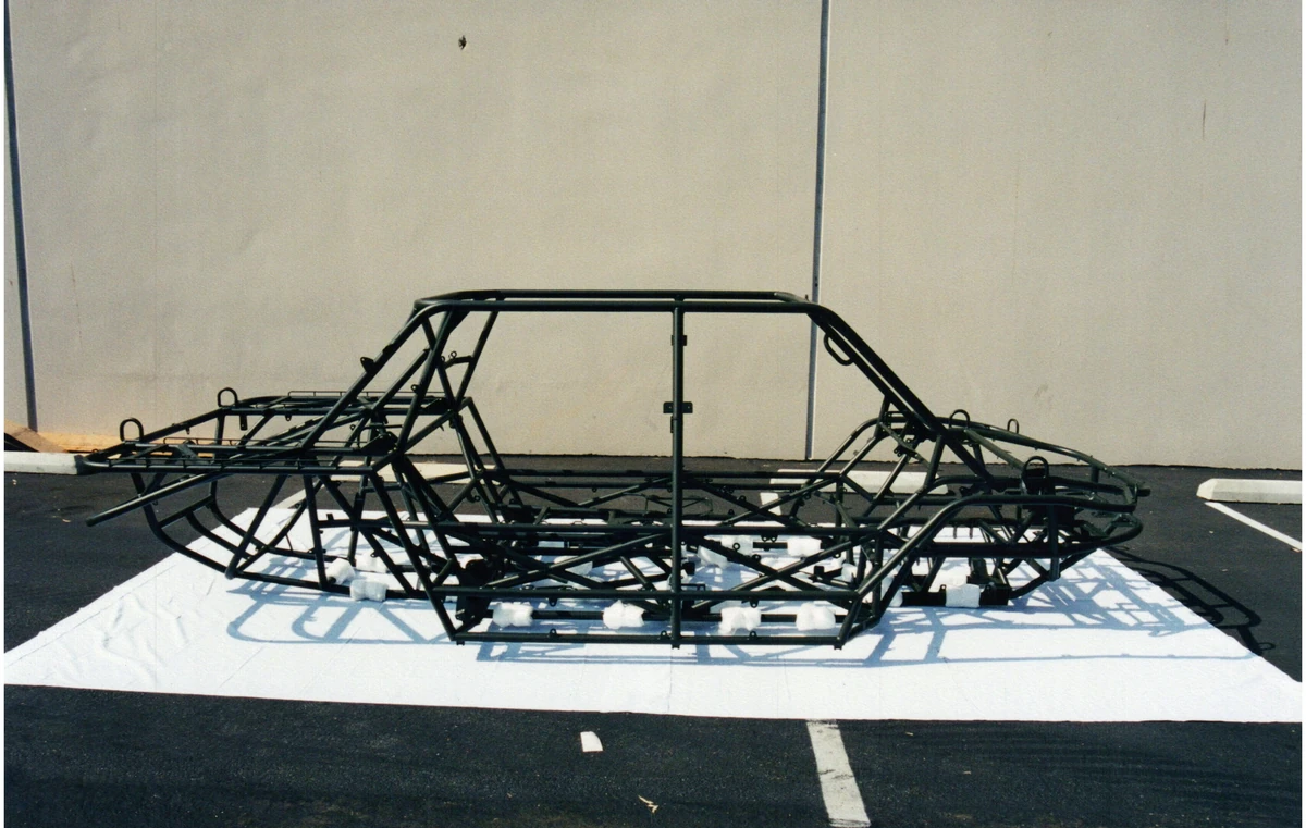 A tubular vehicle chassis resting on a white sheet outside a building