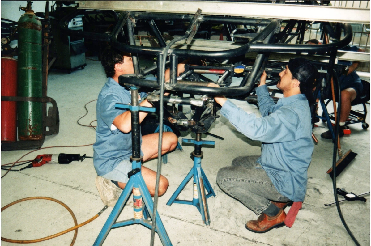 Workshop technicians assembling a tubular vehicle chassis on stands