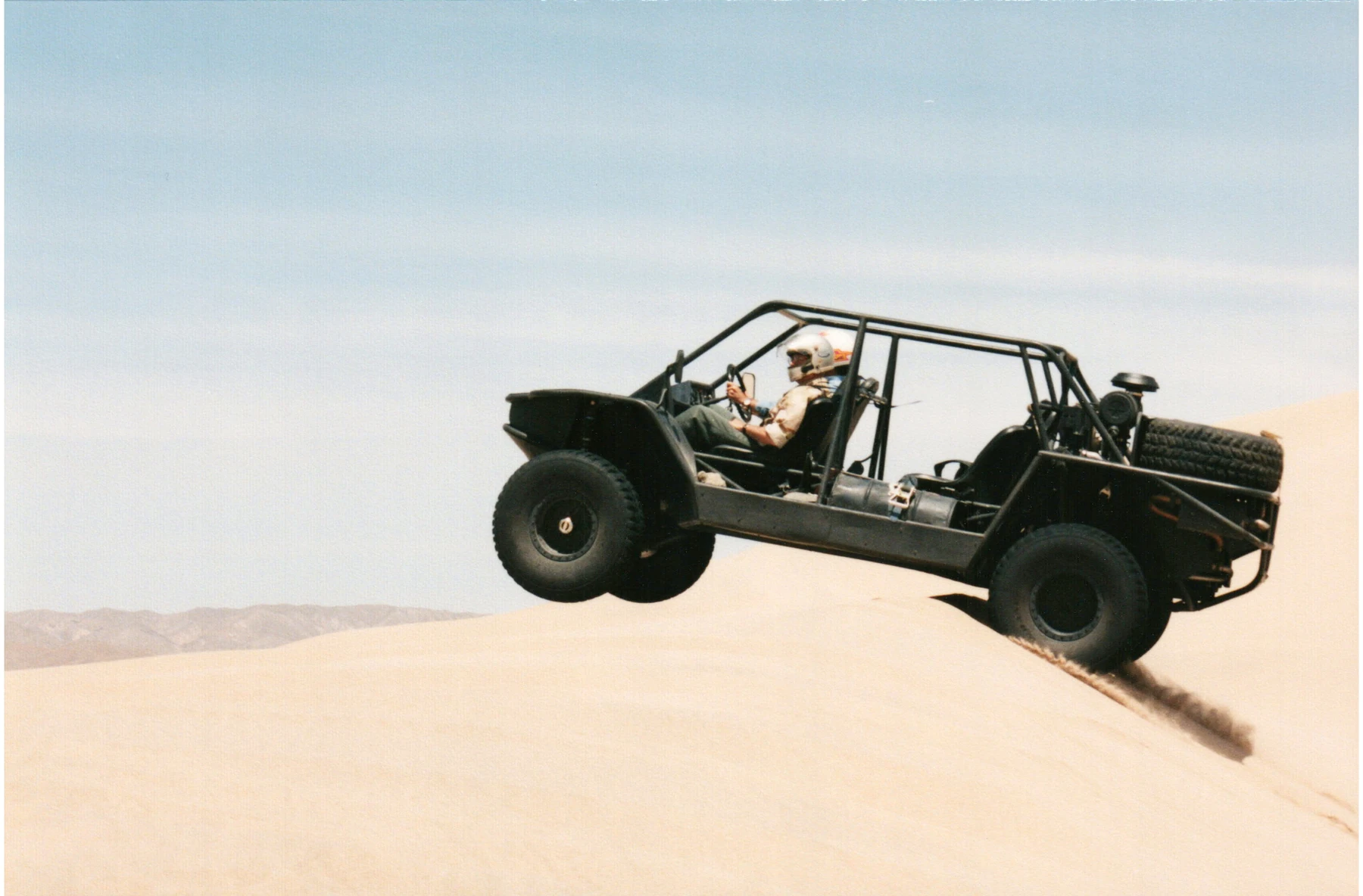 A helmeted driver taking a Flyer vehicle over a sand dune