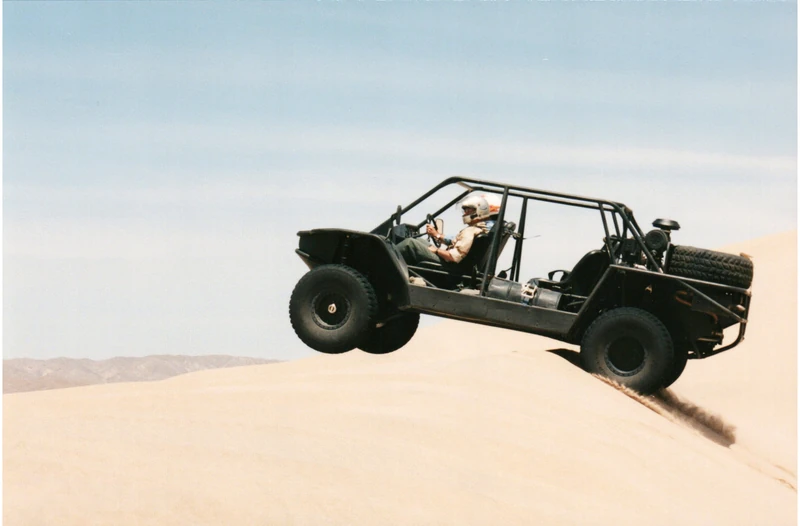 A helmeted driver taking a Flyer vehicle over a sand dune
