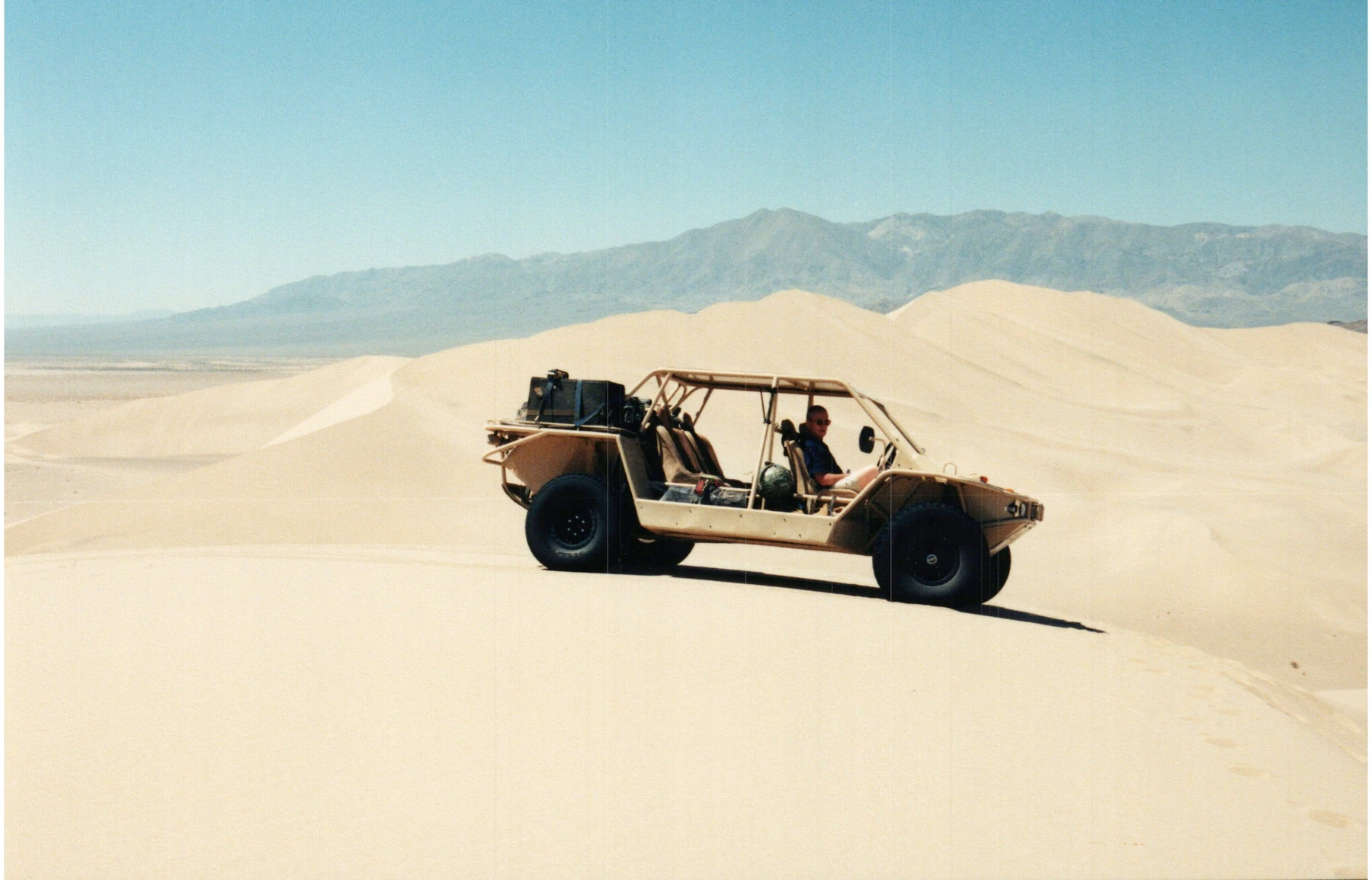 A tan open-cab vehicle photographed among desert dunes