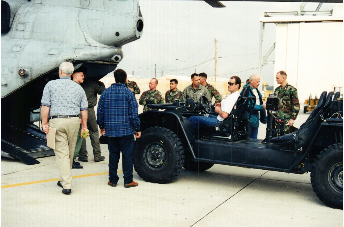 A group gathered around an open-cab vehicle beside the rear of a helicopter