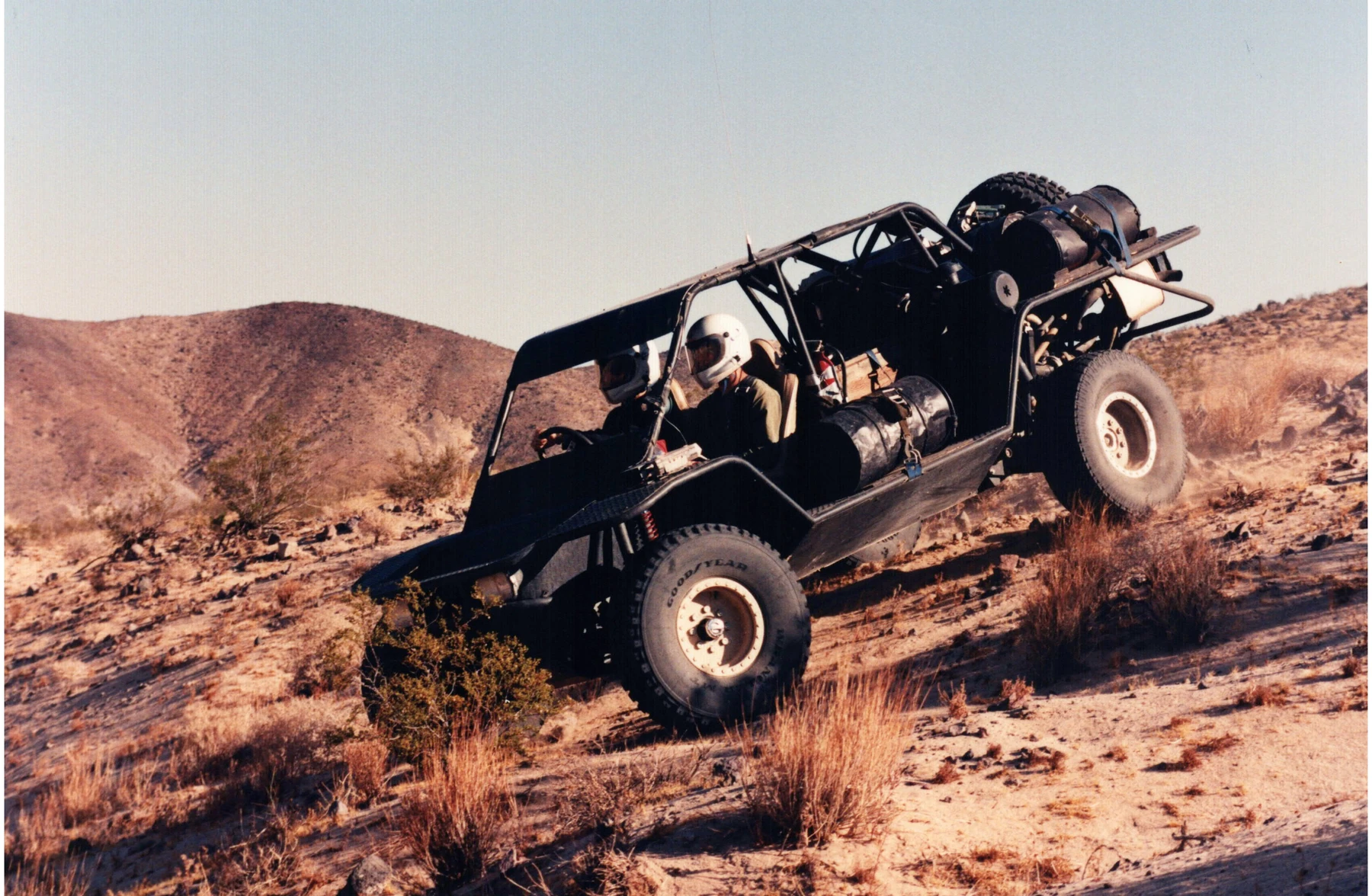 A helmeted driver steering an open-cab vehicle down a dirt hillside