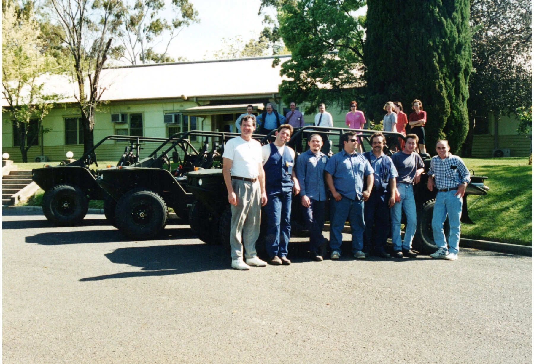 A group gathered beside open-cab vehicles outside a workshop