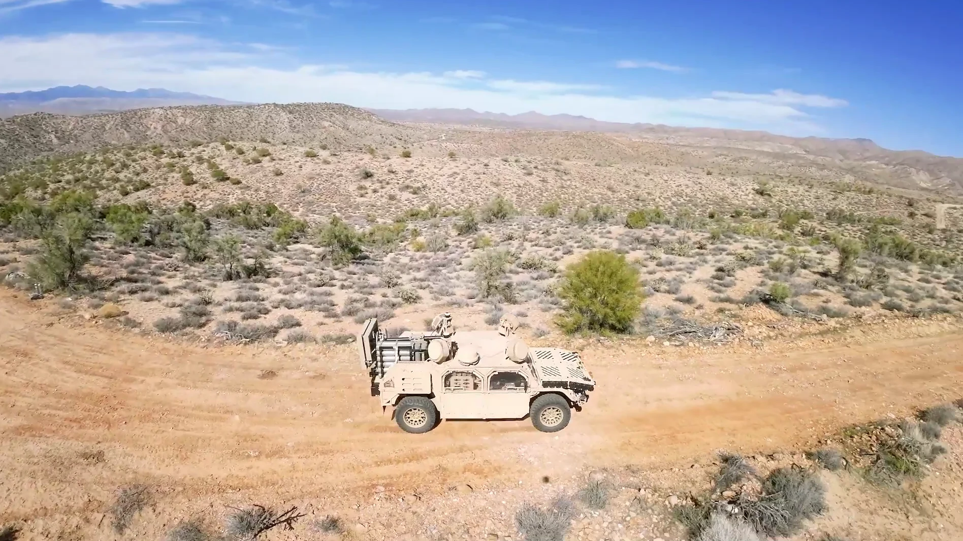 The Beast, a Flyer 72 carrying a 120mm mortar system, drives a desert dirt road, seen from a drone