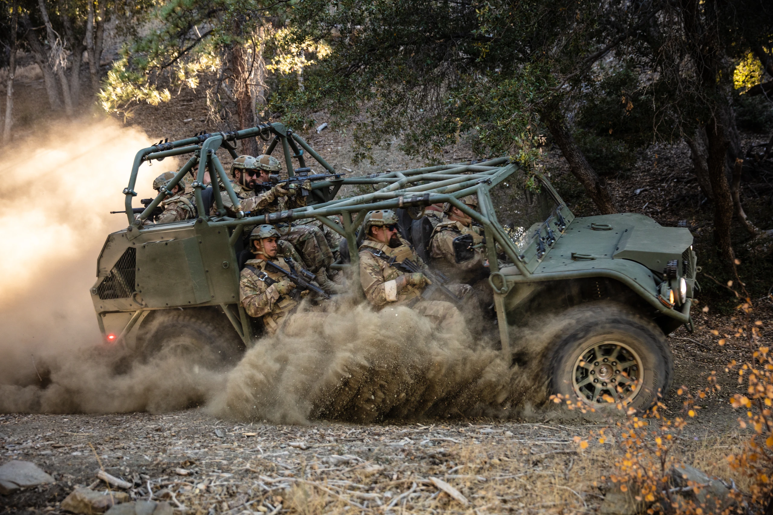 A green Flyer ISV carrying a nine-soldier squad kicks up dust on a wooded trail