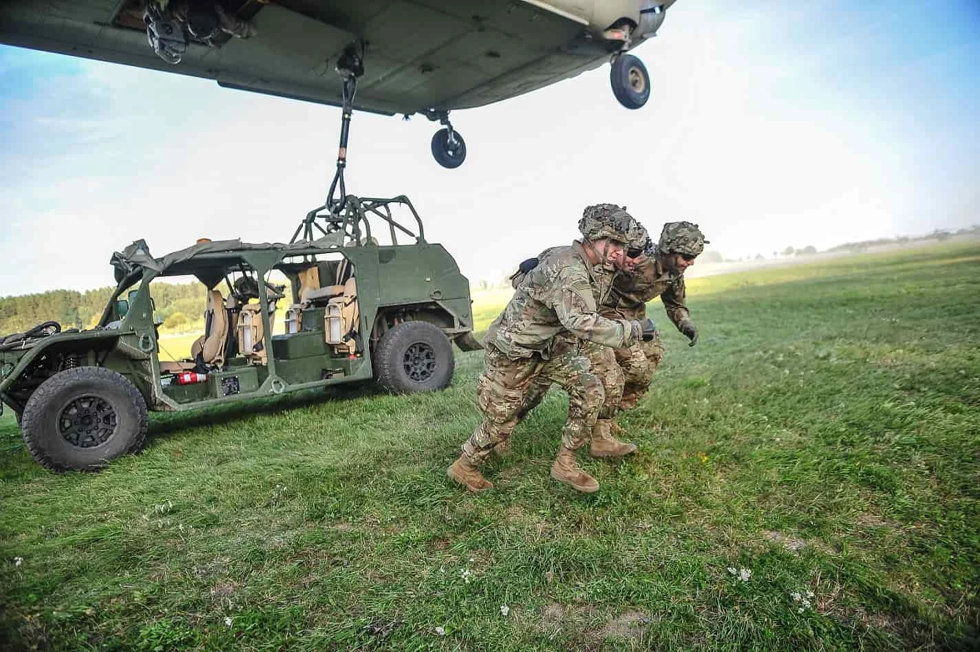 Soldiers move clear as a green Flyer 72 is rigged to a cargo hook under a hovering CH-47 Chinook