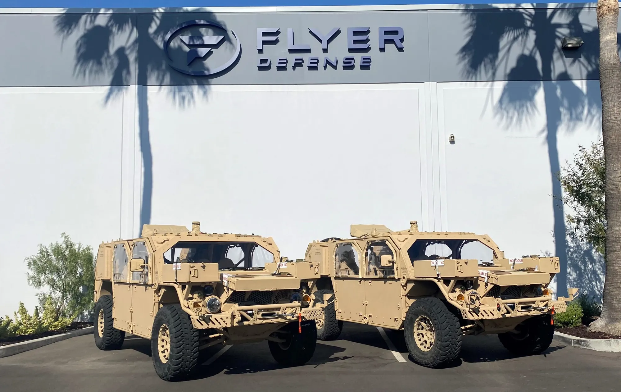 Two tan Flyer 72 vehicles parked outside a Flyer Defense building